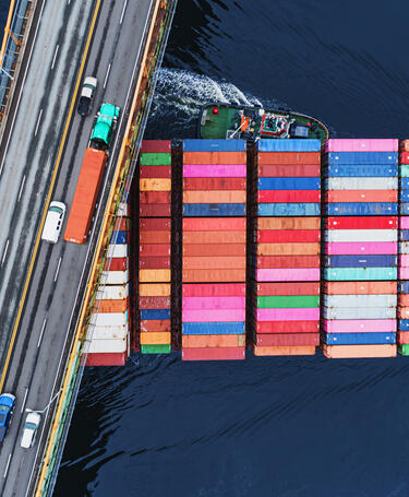 A tanker  of containers travels beneath a busy road bridge