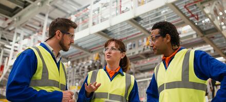 A woman and two men in a factory setting, discussing information on an ipad