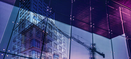 Construction crane and a new high rise building reflected into a newly built office building.